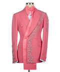 Men's luxury vibrant pink double-breasted tuxedo jacket featuring an innovative asymmetrical extended satin sash, matching oversized bow tie, and heavy pink crystal floral appliqués on the lapel, shoulder, and cuffs