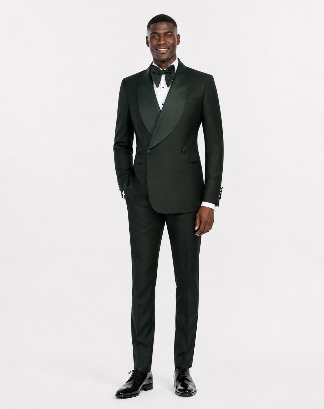 A man modeling a dark forest green double-breasted tuxedo with satin peak lapels, a white dress shirt, a black bow tie, and black dress shoes.
