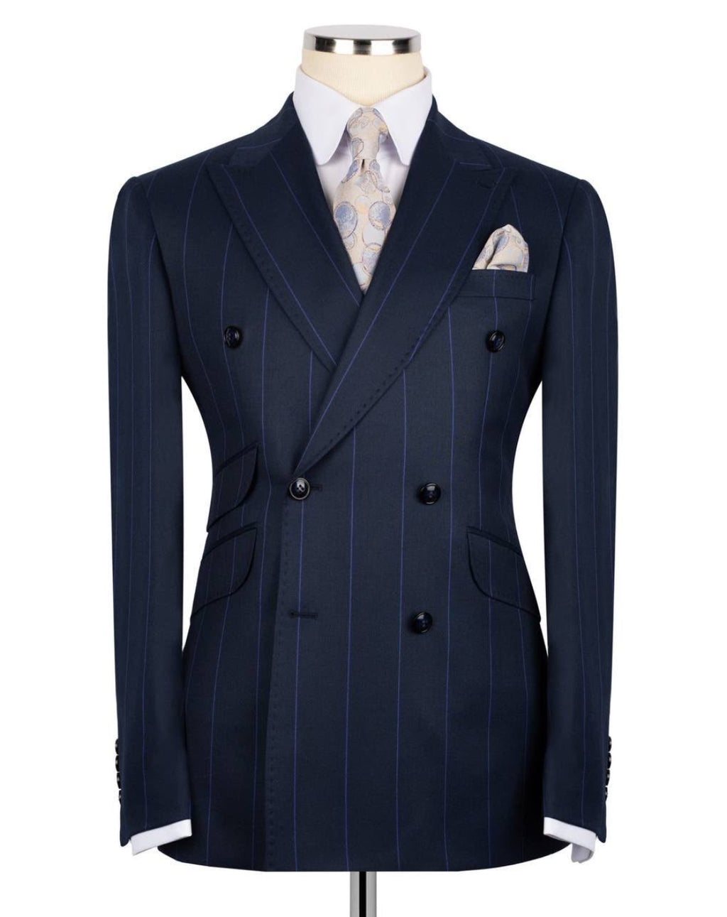 A navy blue double-breasted pinstripe suit jacket displayed on a mannequin torso, styled with a white dress shirt, a patterned beige tie, and a matching pocket square.