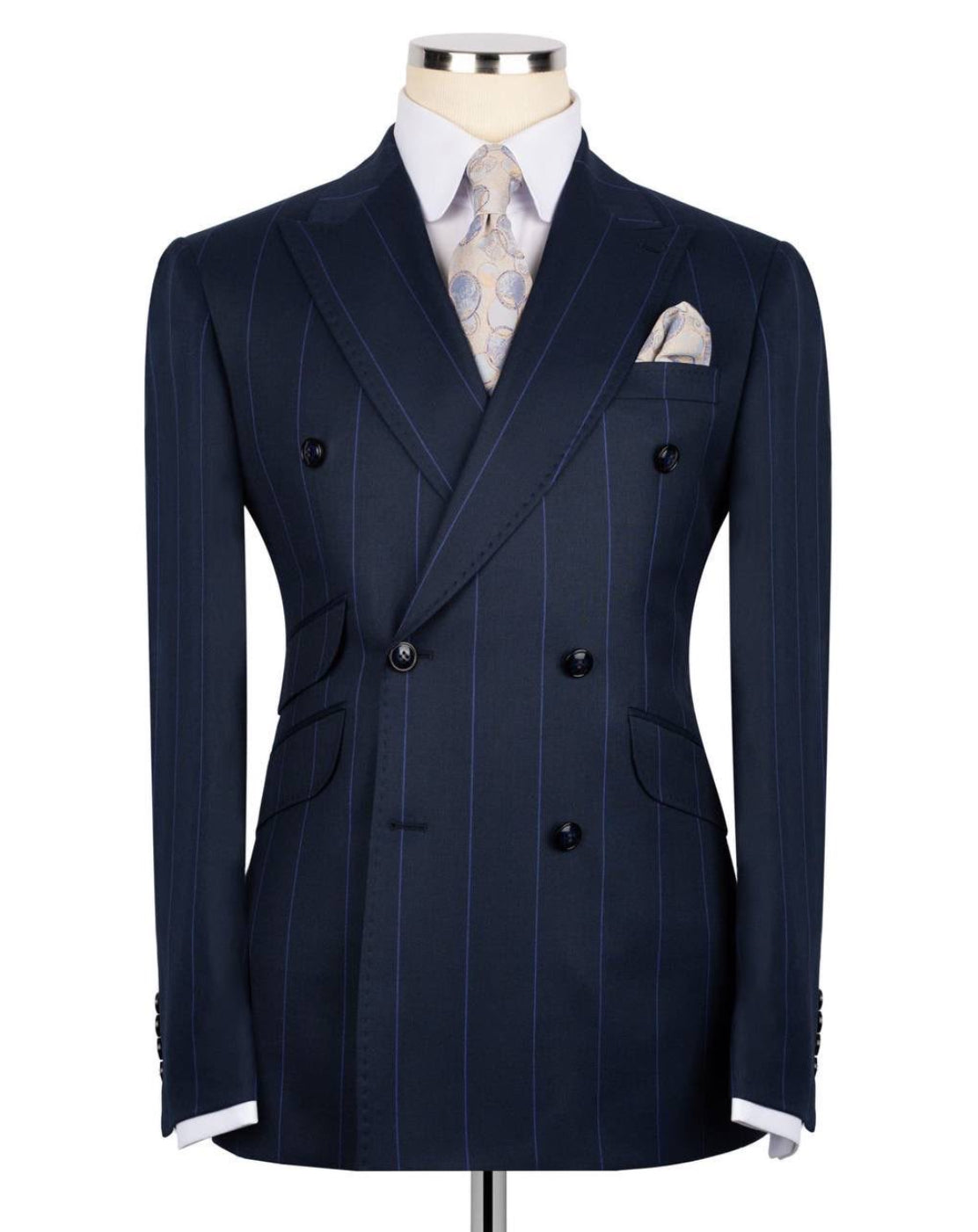 A navy blue double-breasted pinstripe suit jacket displayed on a mannequin torso, styled with a white dress shirt, a patterned beige tie, and a matching pocket square.