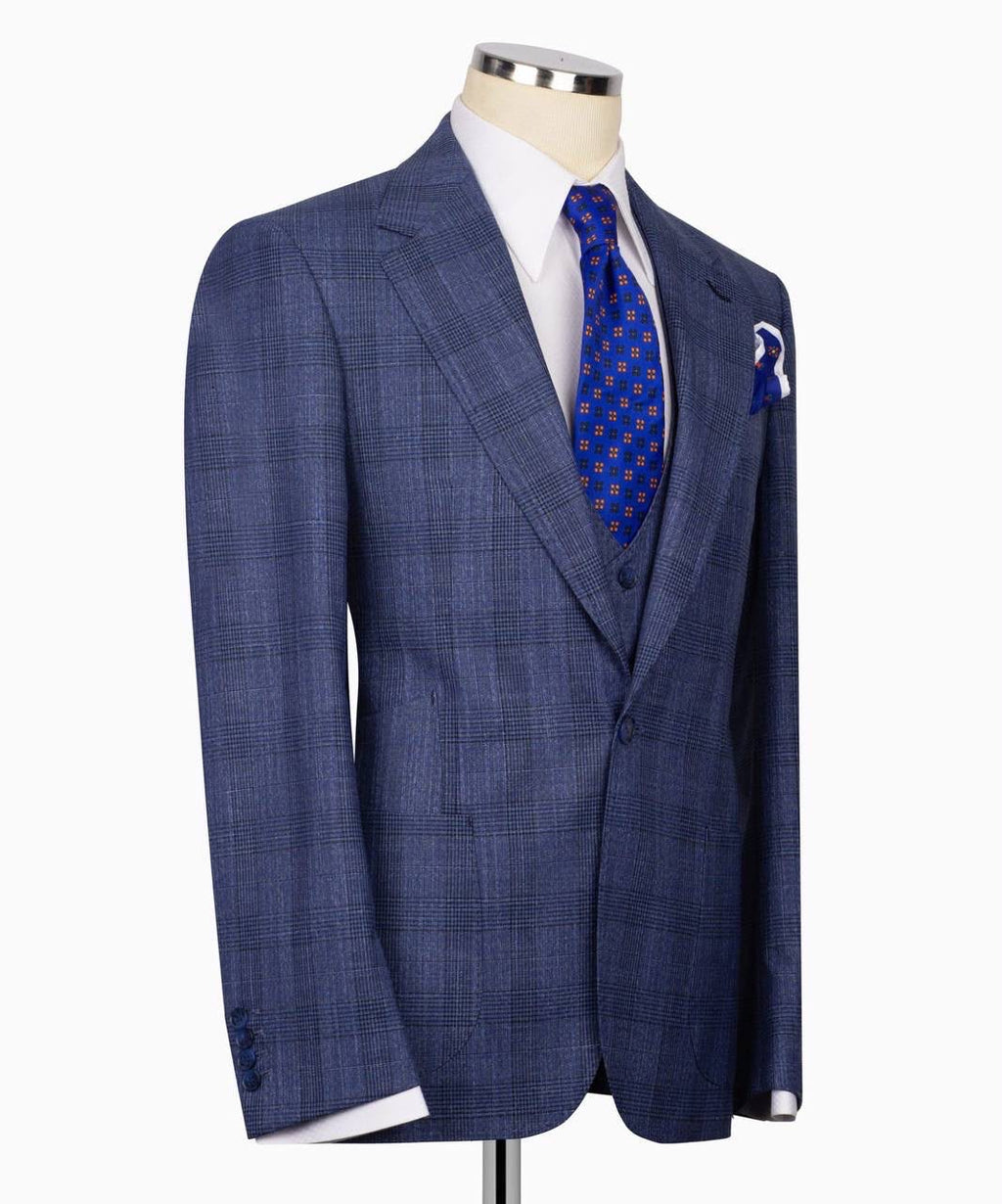 A men's blue plaid suit jacket displayed on a mannequin torso, styled with a white dress shirt, a blue patterned tie, and a matching blue pocket square 