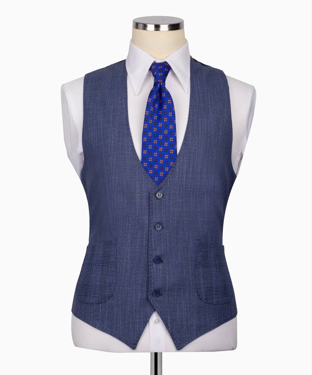 A men's waistcoat displayed on a mannequin torso, styled with a white dress shirt and a blue patterned tie. The waistcoat is a textured slate blue color with a subtle grid pattern and features four front buttons.