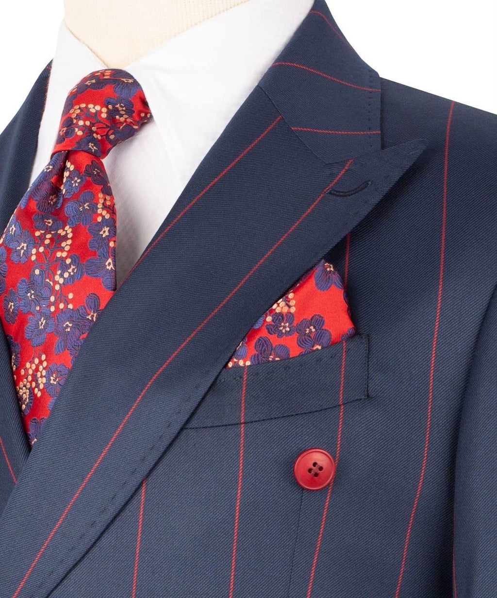 A close-up of a navy blue double-breasted suit jacket with thin red pinstripes, styled with a white dress shirt, a red and navy floral tie, and a matching red and navy floral pocket square.