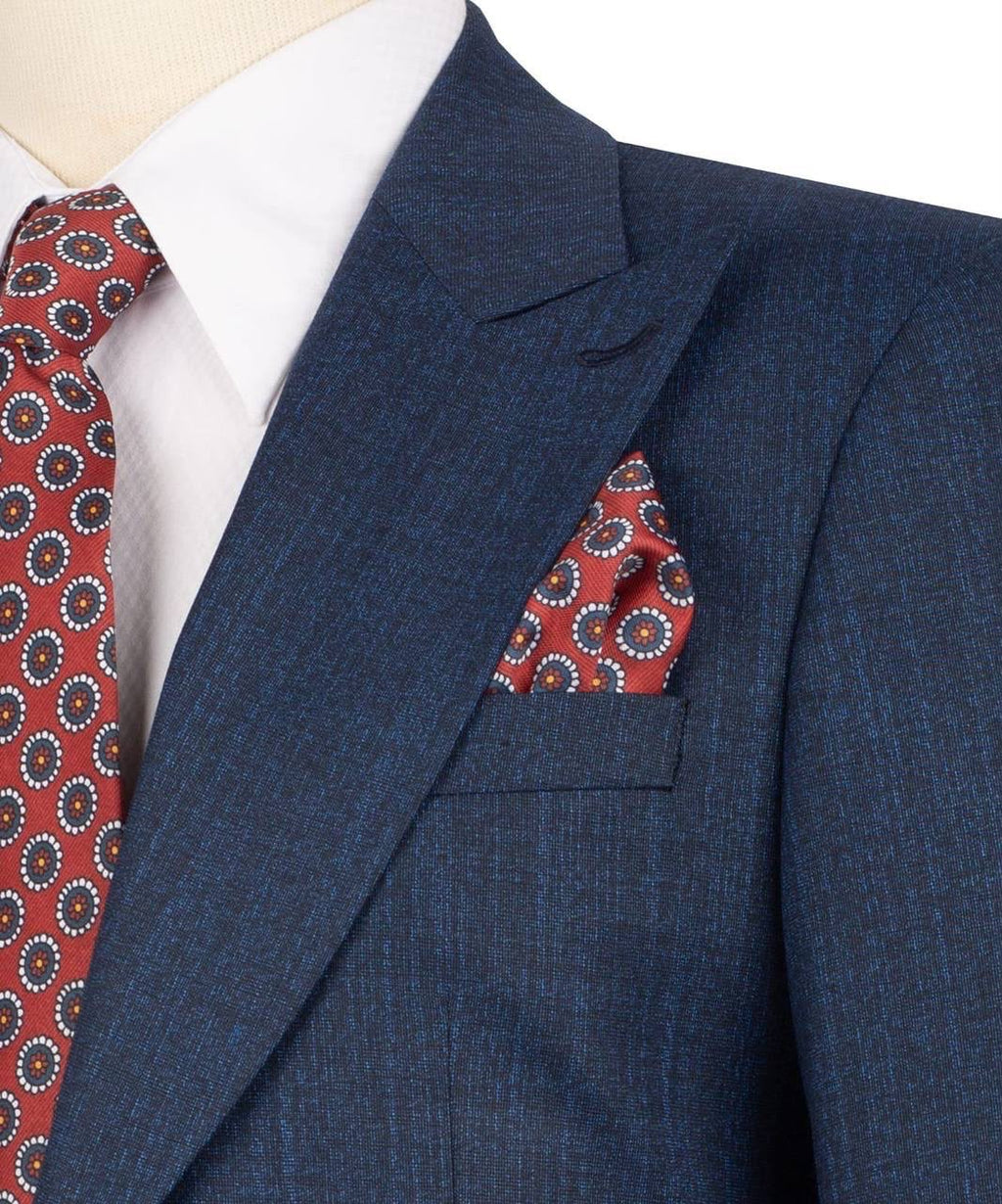 A close-up of a navy blue textured suit jacket worn with a white dress shirt, a red patterned tie, and a matching red patterned pocket square.