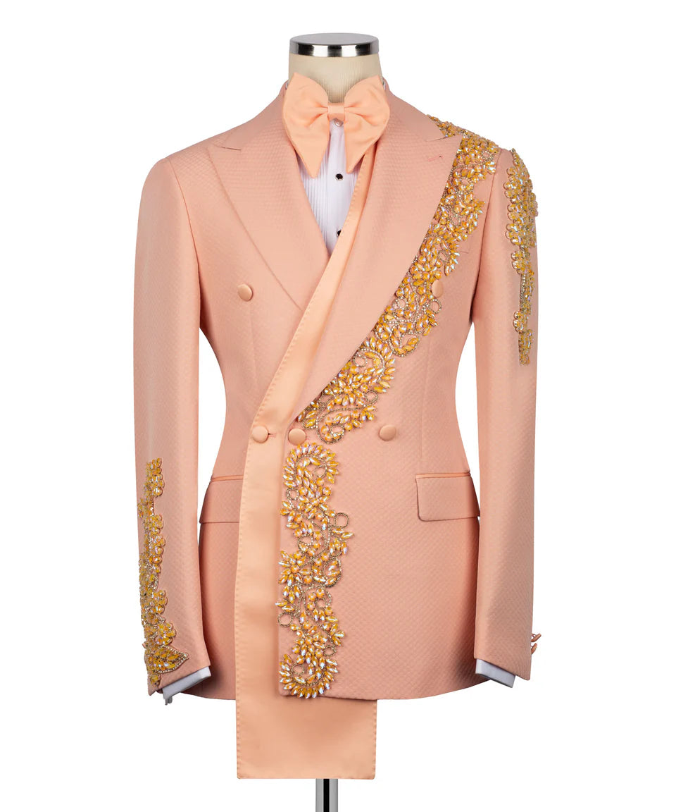 Men's luxury double-breasted tuxedo jackets shown in midnight black and pastel peach, featuring an innovative asymmetrical extended sash and heavy gold crystal floral appliqués on the lapel, shoulder, and cuffs