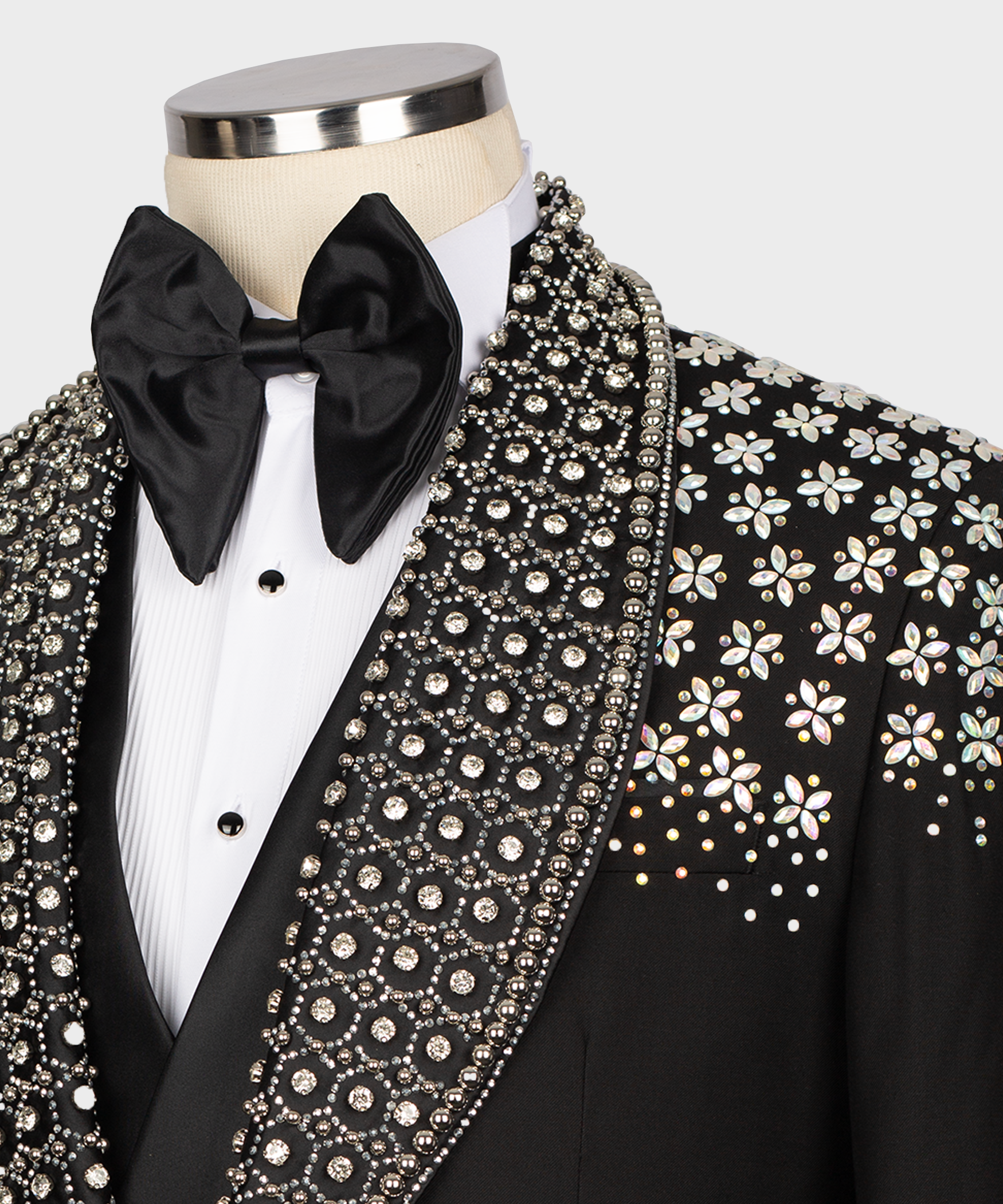 Close-up: black tuxedo bow tie, studded white shirt front, and stone-embroidered lapel trim