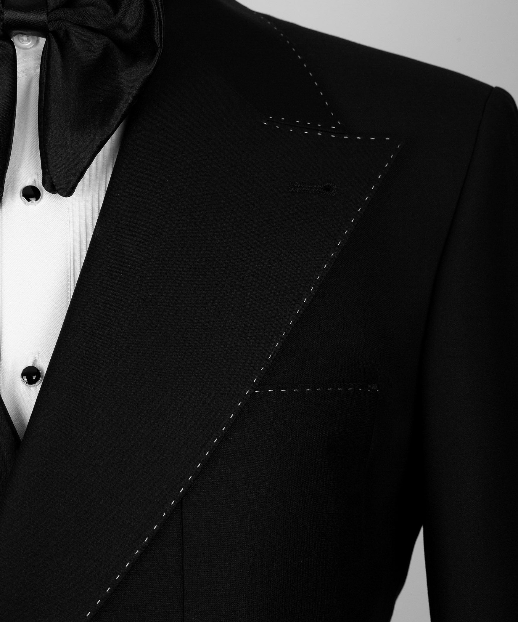 Close-up of black tuxedo lapel with white stitched trim and satin bow