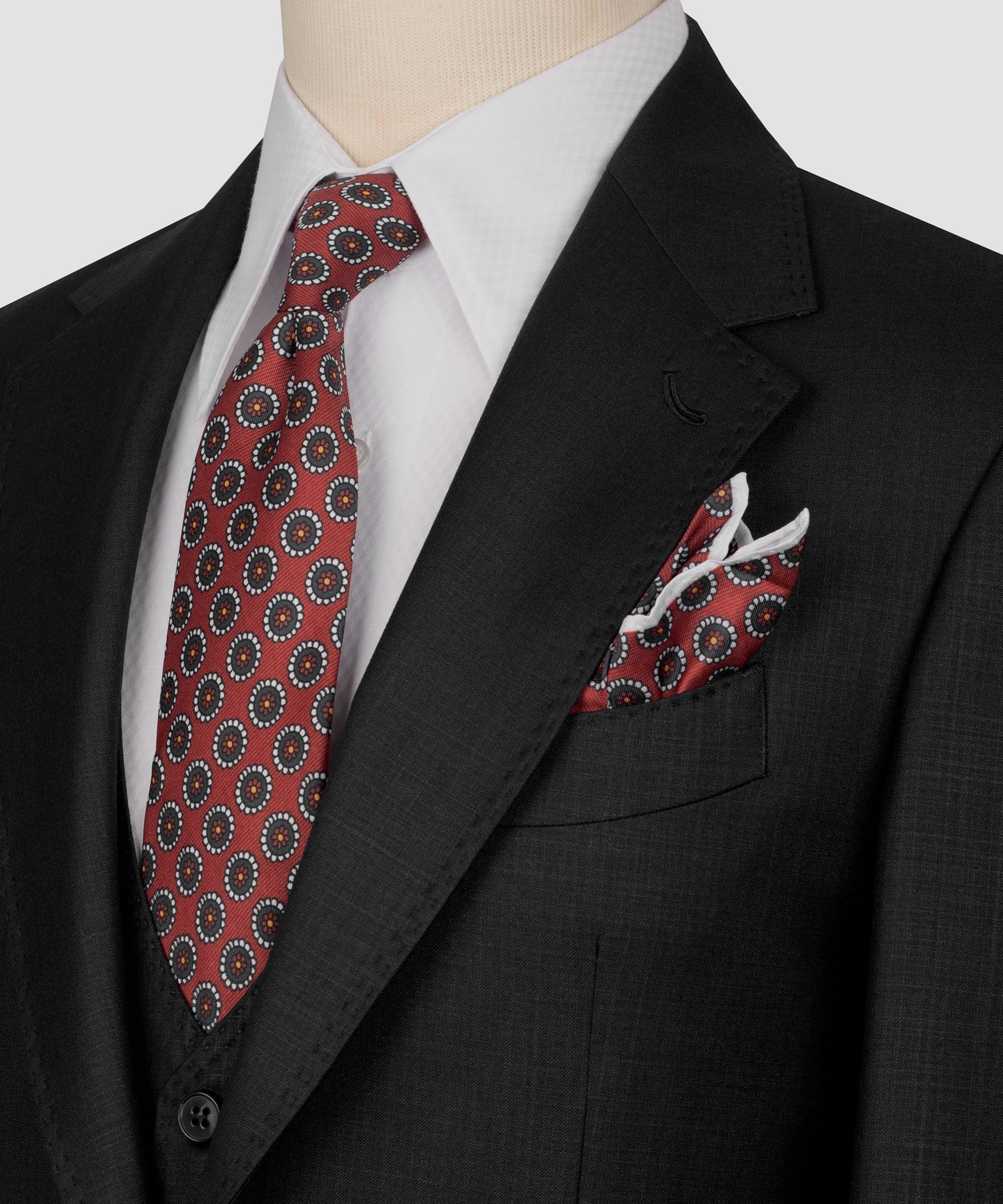 Close-up of black suit jacket lapel with red patterned tie and matching pocket square.