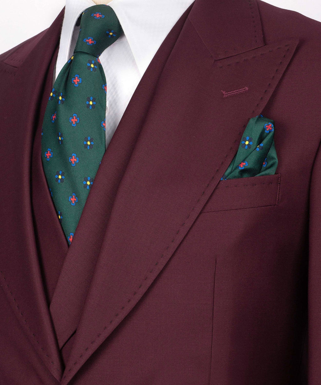 Close-up burgundy blazer lapel with green patterned tie and matching pocket square.