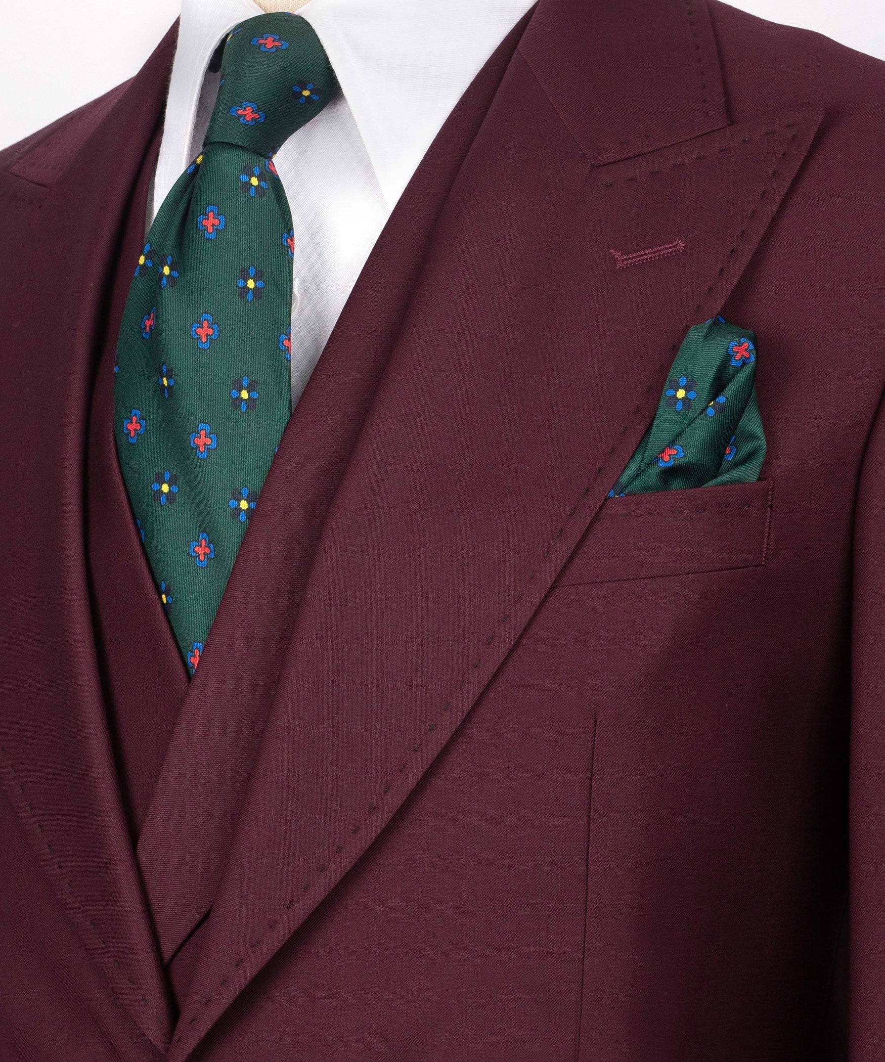 Close-up burgundy blazer lapel with green patterned tie and matching pocket square.
