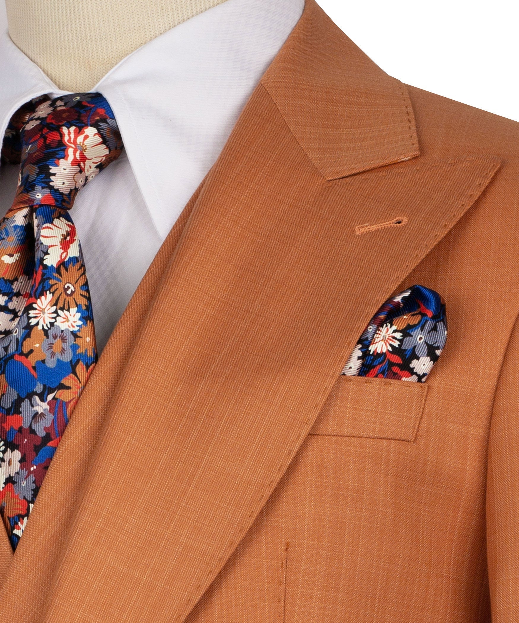 Rust-orange blazer lapel detail with floral pocket square and patterned tie