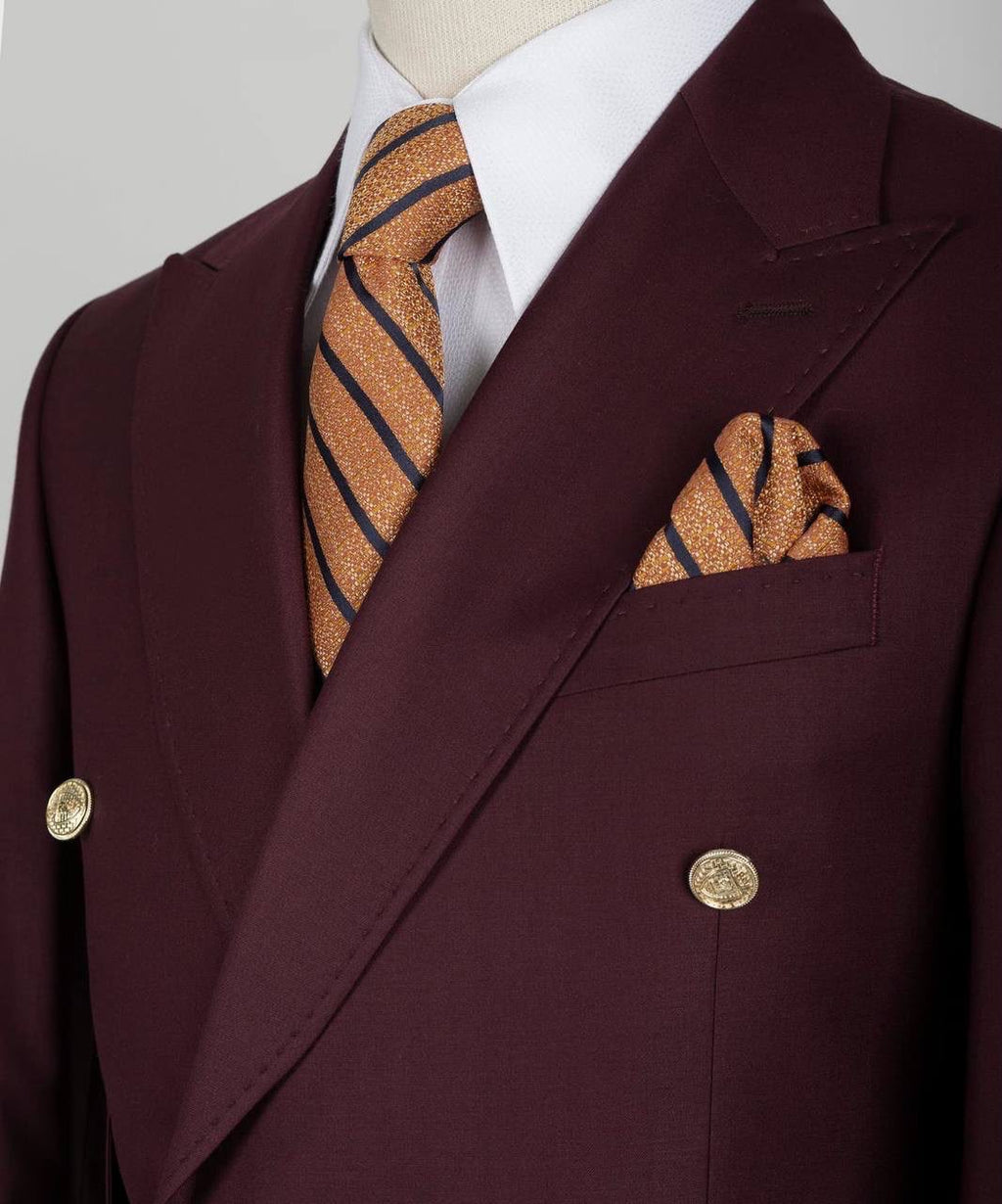 A close-up of a double-breasted suit jacket in deep burgundy, styled with a white dress shirt, a gold-striped tie, and a matching pocket square.