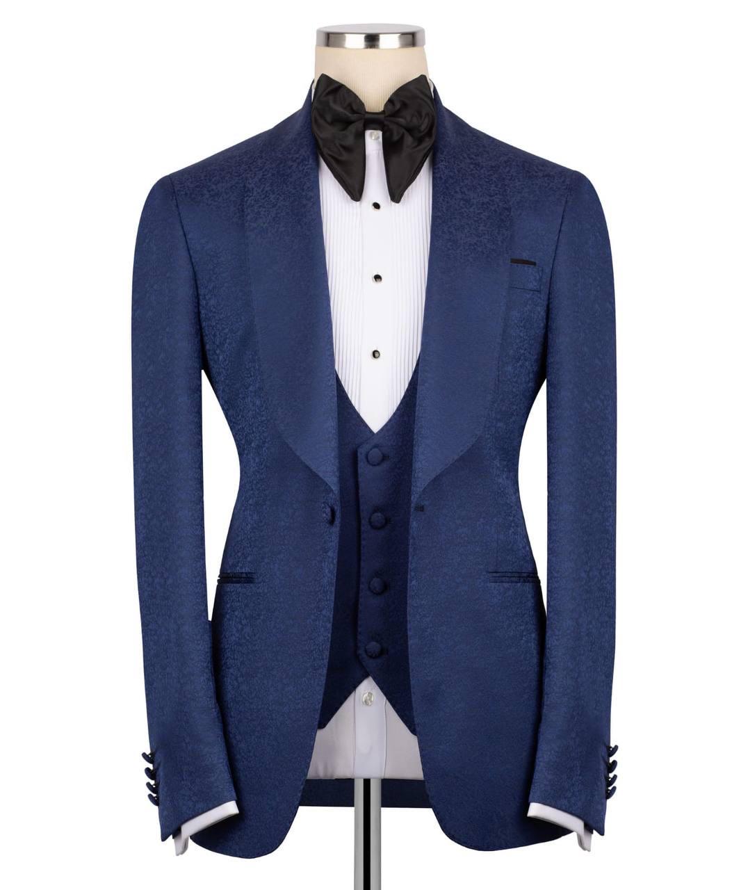 A men's formal tuxedo jacket set in textured navy blue fabric, styled on a mannequin with a white pinstripe shirt, matching navy vest, black bow tie, and white cufflinks.