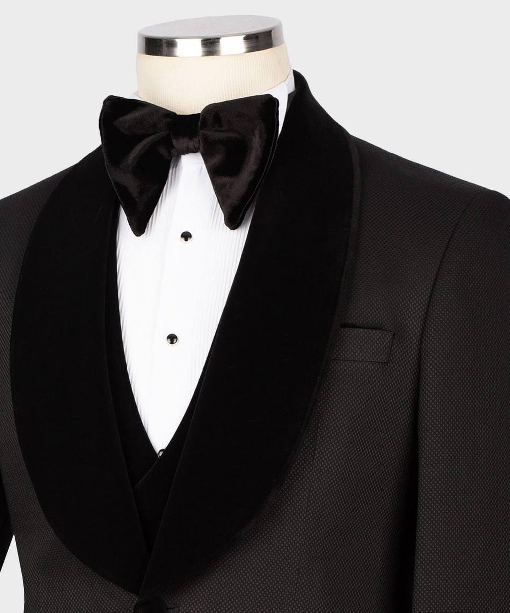 A close-up of a black tuxedo jacket with satin shawl lapels, paired with a matching black velvet bow tie and a white pinstripe dress shirt on a mannequin torso.