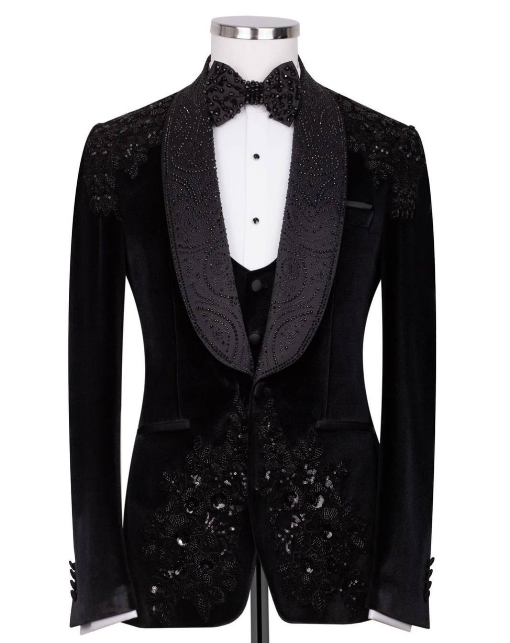 A black velvet tuxedo jacket with ornate beaded and sequined lapels and front panels, displayed on a mannequin with a white dress shirt, black vest, and matching bow tie 