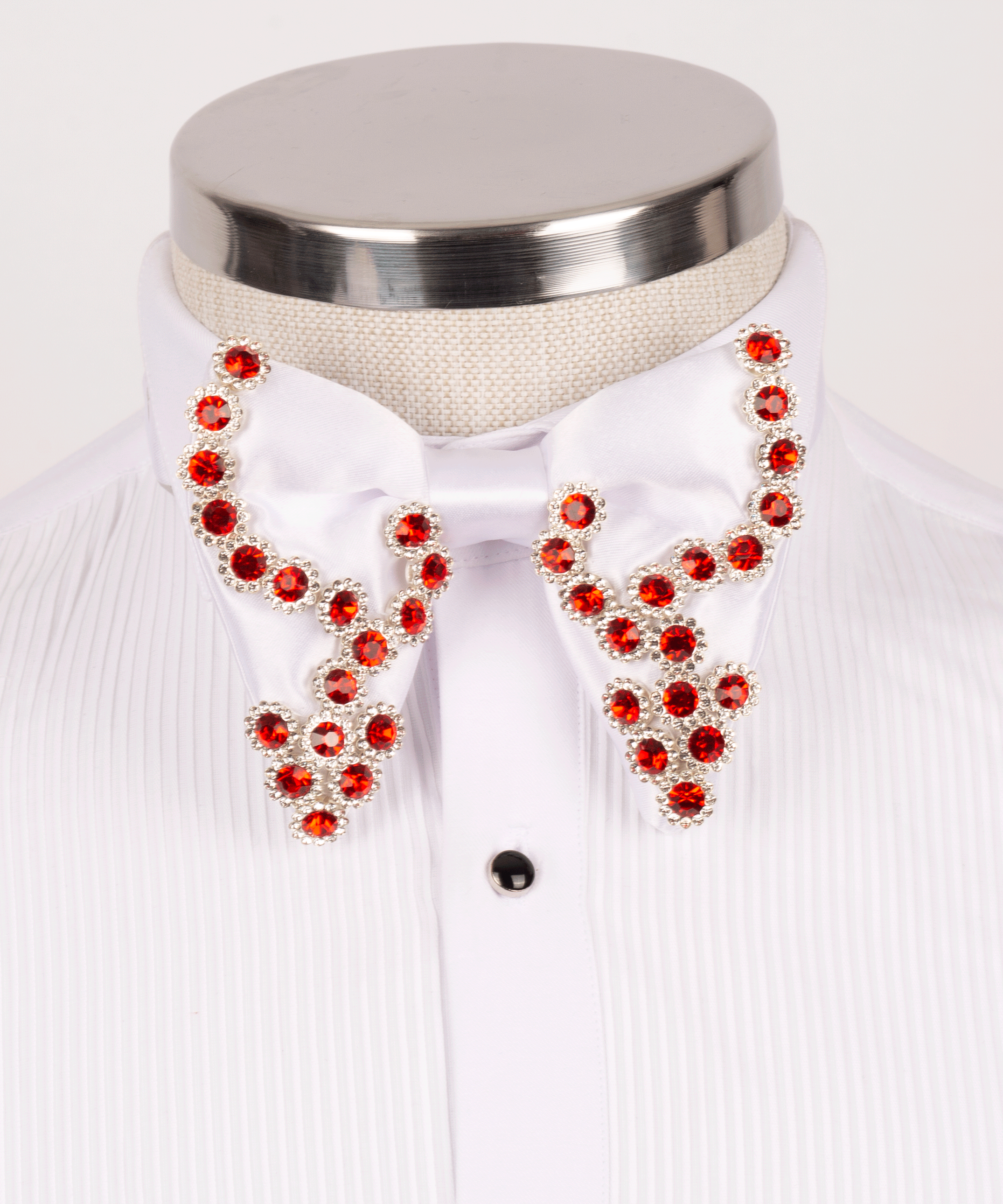 Close-up of a luxury men's white satin bow tie embellished with red crystals, styled on a Koss Atelier pleated tuxedo shirt with black studs.