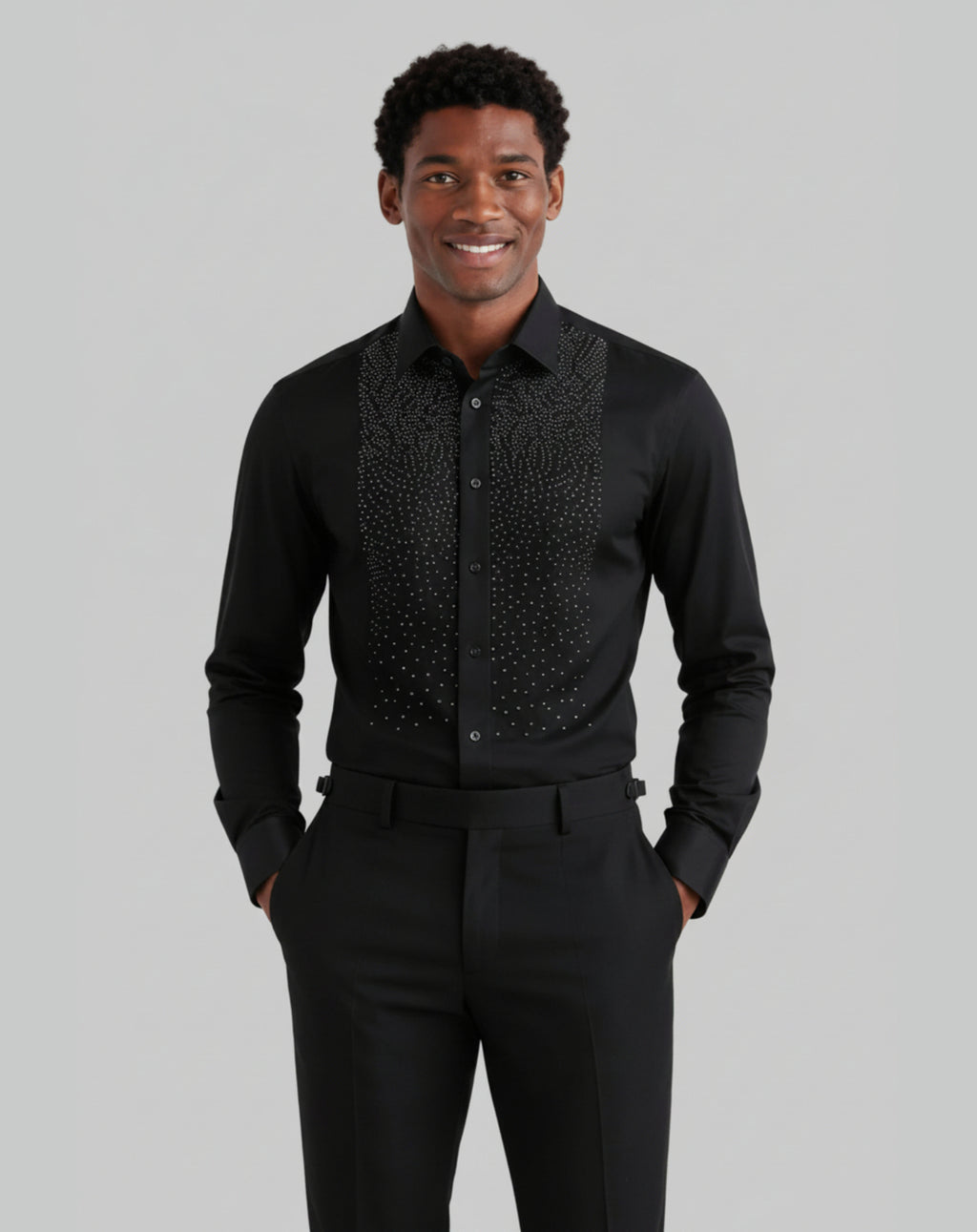 A man wearing a black long-sleeve dress shirt with a textured, patterned yoke and matching black trousers, standing against a solid gray background.