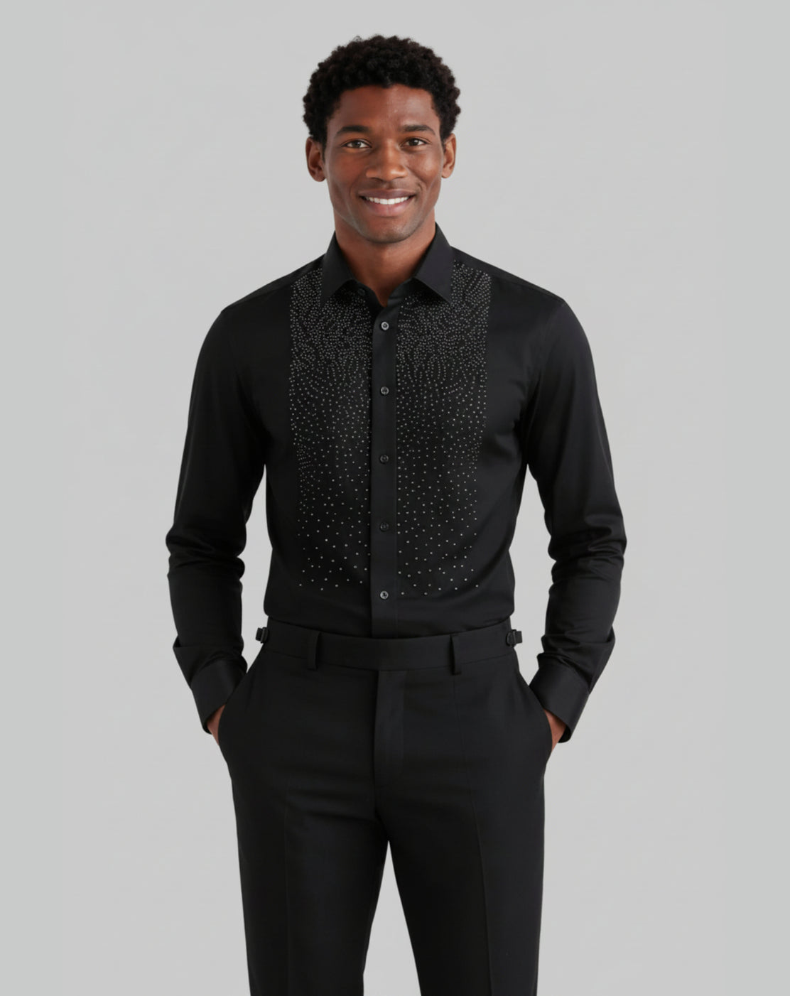A man wearing a black long-sleeve dress shirt with a textured, patterned yoke and matching black trousers, standing against a solid gray background.